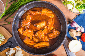 Braised pork ribs in spicy sauce in a large skillet on the table with ingredients - Mexican and Caribbean cuisine