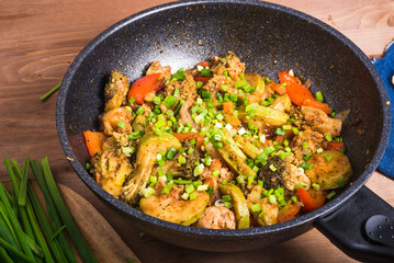 Fried, stewed, cooked, fresh vegetables in a modern wok, sprinkled with chopped spring onions, on a wooden table, close-up - vegetarian healthy cuisine
