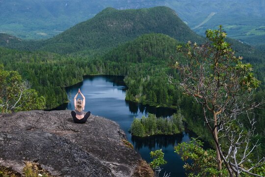 Woman meditating on rock above blue lake. Lily Lake in Madeira park near Sechelt. Sunshine Coast. British Columbia. Canada