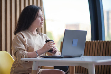 Young hipster woman sitting in coffee, drinking coffee and using laptop.On table is laptop. Girl browsing internet, chatting, blogging.