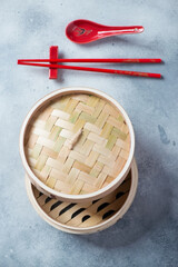 Bamboo steamer with red eating sticks and a spoon on a light-blue stone background, vertical shot, view from above
