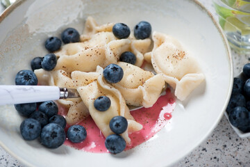 Close-up of vareniki or dumplings with cottage cheese served in a beige plate with fresh bilberry, selective focus