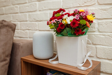 Beautiful autumn bouquet of multicolored chrysanthemums in white paper bag with ribbons in modern interior. Music column or speaker near.