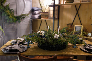 Rustic style Christmas festive table, blue glasses, plates and fresh thuja, fir branches, cotton bouquet with candles. Eco-friendly green decorative elements.