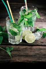 Mojito cocktails on a rustic wooden desk background. Two natural mojito cocktails with mint leaves, ice cubes, and lime on a wooden table.