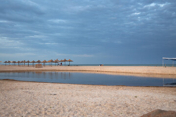 A sparsely populated beach with straw umbrellas at the end of the swimming season on the south coast.
