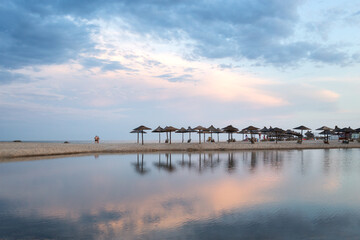 A sparsely populated beach with straw umbrellas at the end of the swimming season on the south coast.