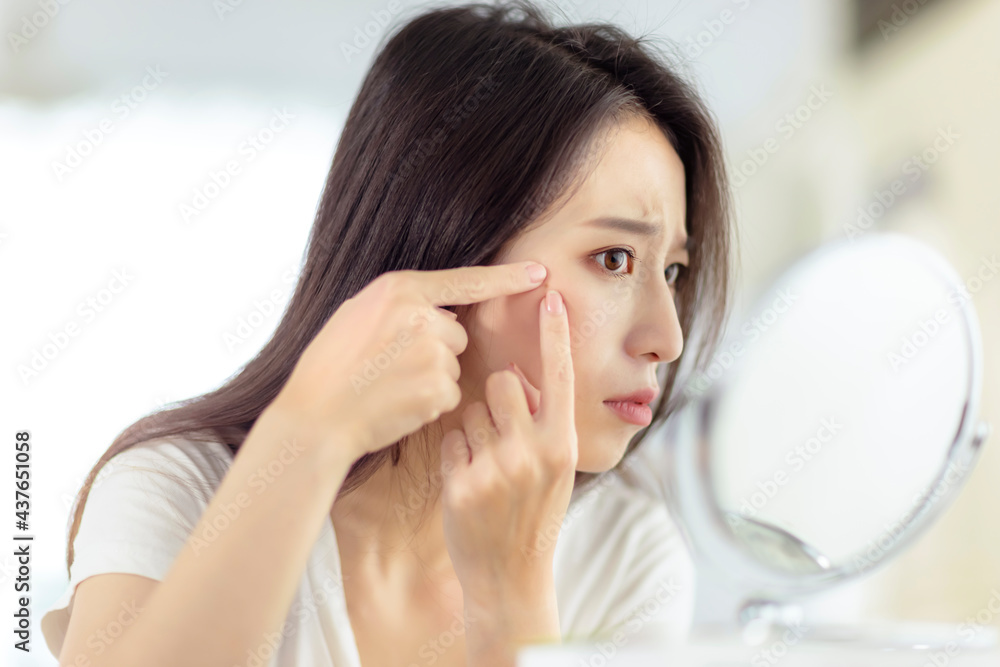 Wall mural Young woman looking at  mirror and checking the  acne problem at home