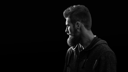 Black and white shot of profile young handsome serious bearded man isolated on black background