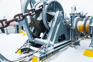 The mooring deck of a cargo ship with anchor winches, an anchor chain on winches, bollards and haws with mooring ropes, frozen and covered in snow. Snow on the mooring deck of a cargo ship.