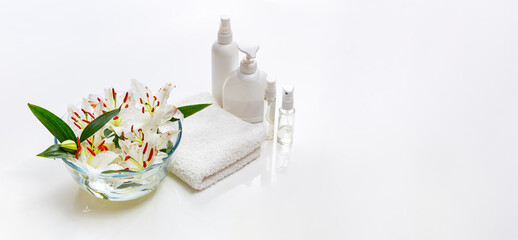 White spa towel with body care bottles and bowl with white lilies.