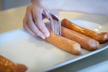 Close-up hands use fork puncturing homemade sausage.