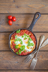 Shakshuka - fried eggs with vegetables in iron cast on wooden table