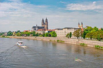 View over old cathedral at historical downtown in Magdeburg with a touristic boat with name of Saxony Anhalt coming by at Elbe river, Germany, at blue summer sky with clouds. - obrazy, fototapety, plakaty