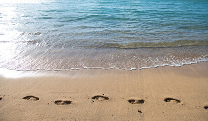 Beach background footprints in sand foot print. Concept for travel vacation. Footsteps in sand on summer tropical getaway holidays vacation with blue ocean.