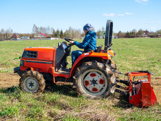 Obraz premium The girl sits in a small tractor and drives through the field mulching grass. Land cultivation, agrotematics