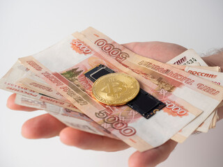 a man's hand holds Russian banknotes, an m2 SSD disk and bitcoin. The concept of earning and mining money on hard media