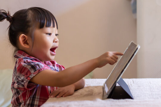 Portrait image of 3-4 years old preschool kid. Happy Asian child girl using and touching smart pad or tablet for do her homework and online learning (E-learning). Back to school, Study frome home. - Powered by Adobe