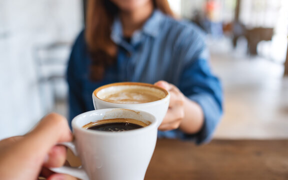 Closeup image of a woman and a man clinking coffee cups together in cafe