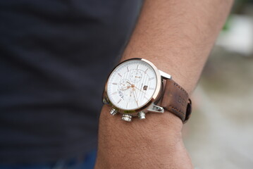 A white analog watch with brown band in wrist