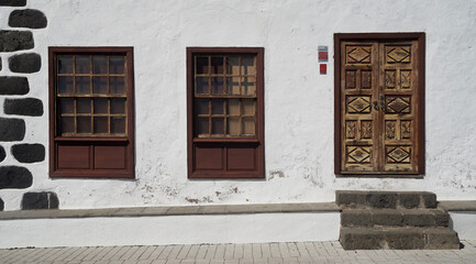Picturesque facade of a traditional stone house. White whitewashed wall. Wooden ornate carved door and windows. La Palma, Canary islands