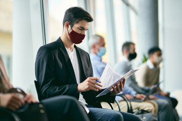 Businessman wearing face mask and going through paperwork while waiting for job interview.