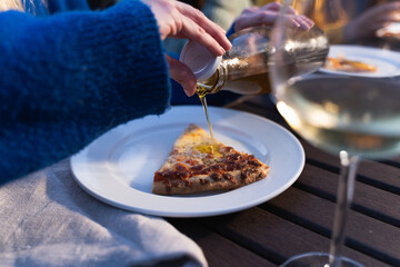 Unrecognized woman enjoying her dinner and pouring olive oil in her pizza.