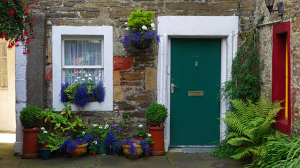 Fototapeta na wymiar Picturesque facade of a traditional stone house with ornate colored green door and white window. With many pots and flowers in front. kirkwall, scotland