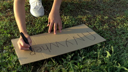 The girl writes anywhere with a marker on cardboard. Hitchhiking. Trying to stop the car with a sign