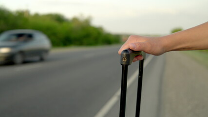 Close-up of a woman holding a handle in a suitcase against the background of passing cars on the highway