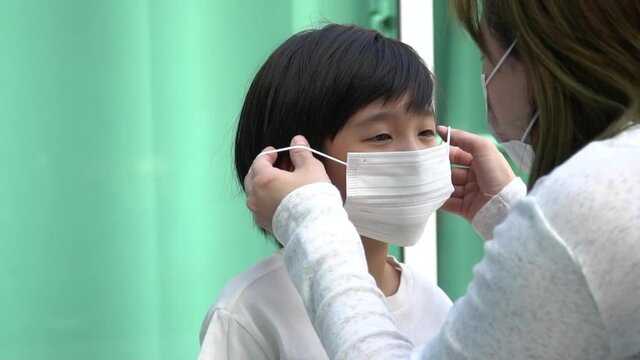 Asian mother puts a safety mask on her son face