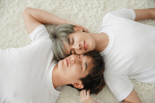 Top view of young Asian gay couple closed their eyes and lying on floor with white fluffy carpet. Their men face are very close together and they touch each other hairs while sleeping. 