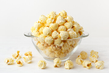 Fresh, sweet popcorn with golden caramel in a glass bowl on a white wooden table