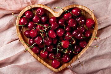 Ripe sweet cherries on a wooden plate in the shape of a heart on a pink background top view