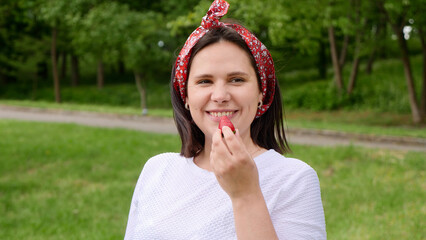 Fototapeta premium Girl eating strawberry, smiling happy, looking at camera. Young woman eating red strawberry berry. Portrait of mom, housewives, farmer