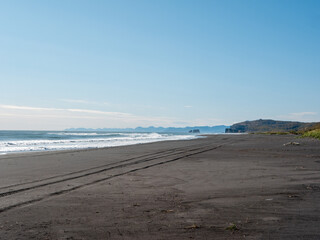 View from the Khalaktyrsky beach to the Pacific Ocean against the background of the blue sky. On the horizon of the black sand beach, cliffs and ocean waves are visible. Kamchatka Peninsula, Russia.