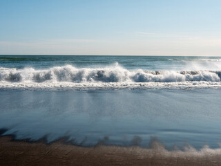 View from the Khalaktyrsky beach to the Pacific Ocean against the background of the blue sky. On the shores of the black sand beach, big and small waves break. Kamchatka Peninsula, Russia.