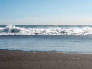 View from the Khalaktyrsky beach to the Pacific Ocean against the background of the blue sky. On the shores of the black sand beach, big and small waves break. Kamchatka Peninsula, Russia.