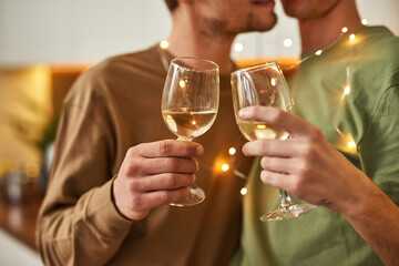 Same-sex male partners kissing while holding wine glasses