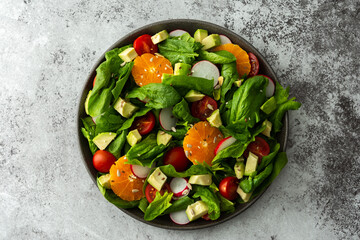 Delicious healthy salad of spinach leaves, tangerine and avocado slices, tomato and radish with seeds, salad in a plate close-up ,top view, copy space