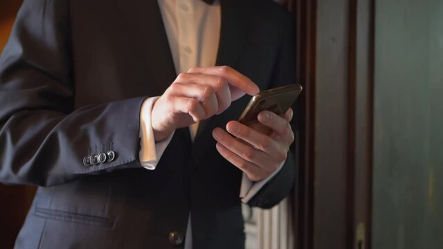 A man in a business suit types text on his smartphone. 