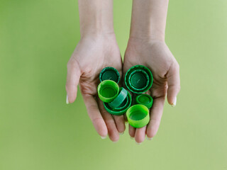 Top view of hands holding plastic bottle cups on bright green and turquoise background. Sorting out plastic garbage
