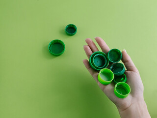 Top view of hand holding plastic bottle cups on bright green and turquoise background. Sorting out plastic garbage