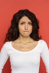 Nervous woman portrait: closeup of unhappy doubtful young female biting lip in doubts, worried of mistake or important event, result announcement. Cute anxious stressed girl isolated on red background