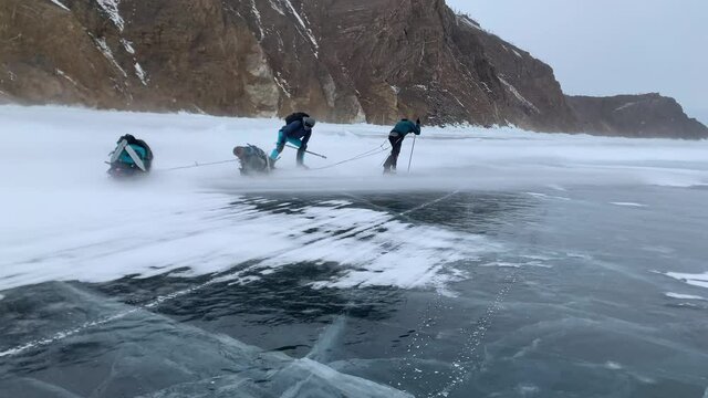 Two men are blown away by a hurricane wind with a blizzard during a hike across frozen Lake Baikal with sledges equipped with backpacks in winter. Storm on Lake Baikal in winter