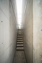 Narrow exposed concrete stair and lighting at the end of small corridor express to minimal style of architecture.