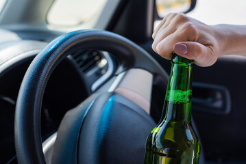 A faceless woman opens a bottle of beer while driving a car. Breaking the law and drinking alcohol...