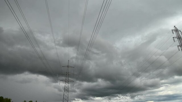 Time lapse view of storm clouds moving over high voltage electric towers. Electricity steel pylon tower. Low angle view of power line. Static shot, wide angle