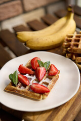 Closeup view of breakfast belgium waffles with strawberry and banana with mint on wooden background. High quality photo