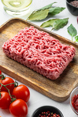 Bolognese sauce ingredients, minced meat tomatoe and herbs, on wooden tray, on white stone  background